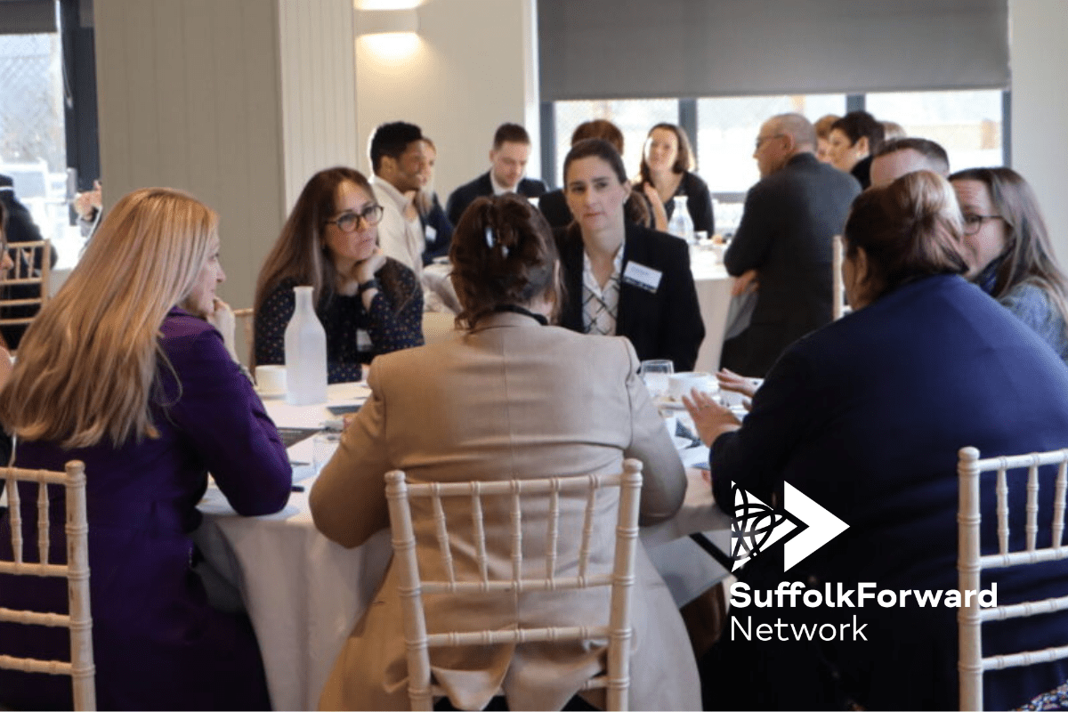 A group of people sit around a table talking in a corporate networking setting.